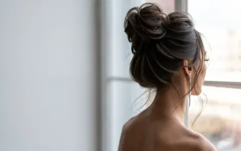 Elegancki kok na głowie kobiety, ozdobiony długimi kolczykami, spogląda przez okno.