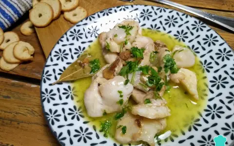 Plato de que son las cocochas de bacalao, tiernas y jugosas, en una salsa amarilla con perejil picado y galletas tostadas al lado.