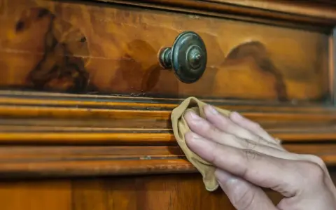 Restauración de mueble antiguo. Mano aplicando betún de judea antes y después, revelando su brillo natural.
