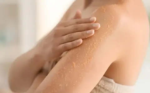 Mano che applica scrub su braccio, rimuovendo la pelle morta dopo la doccia per una pelle liscia e luminosa.
