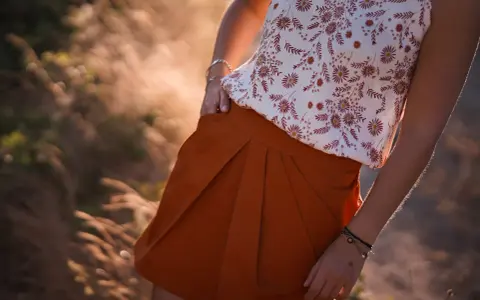 Jupe tulipe orange à plis, portée avec un haut fleuri. Le soleil couchant illumine la scène.