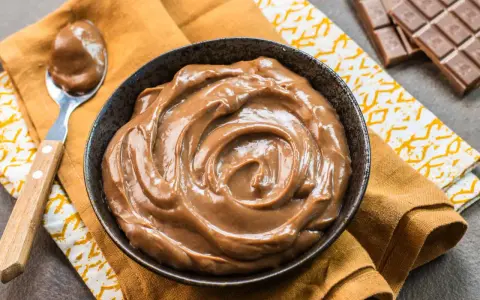 Una ciotola piena di deliziosa crema pasticcera al cioccolato, con una cucchiaiata pronta da gustare. Accanto, una tavoletta di cioccolato.