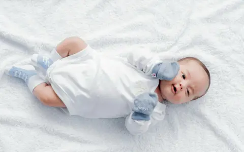 Dolce neonato nel suo primo mese, sdraiato su un soffice telo bianco, con calzini azzurri e guantini.