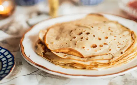 Una pila de masa crepes doradas y finas en un plato blanco.