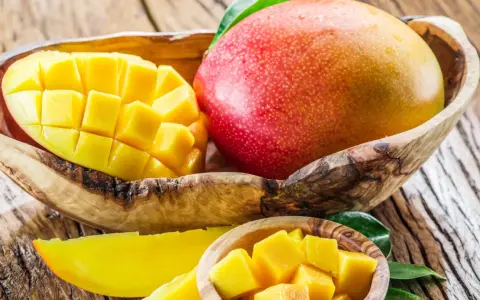 Soczyste, pokrojone w kostkę i w całości mango w drewnianej misce. Owoc ten zawiera mnóstwo witamin.