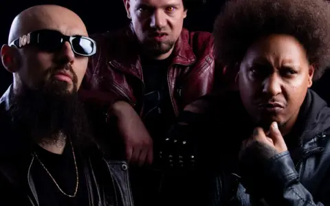 Trois hommes au look sombre, dont un avec des lunettes de soleil et une barbe, un autre avec des yeux jaunes et une veste rouge, et le troisième avec une afro. Un trio dope dod.