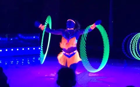 Artistin dreht leuchtende Reifen auf der Bühne des Circus Moreno. Neonfarben und Schwarzlicht erzeugen eine magische Atmosphäre.