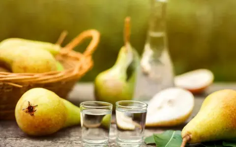 Frische Birnen und zwei Gläschen Schnaps auf Holztisch. Ein Korb voller Birnen im Hintergrund. Perfekt für ein Birnenschnaps Rezept.