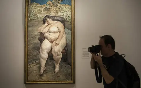 Un hombre fotografía un cuadro de **lucian freud desnudos**, una figura sentada en un sillón, capturando la intimidad de la obra.