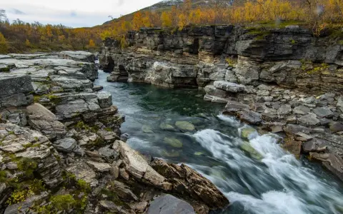 Vatten forsar genom Abisko kanjon, kantad av dramatiska klippformationer och höstens gyllene lövverk.