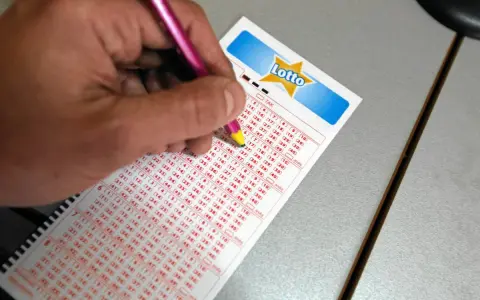 Ręka zaznacza liczby na kuponie Lotto, próbując wybrać szczęśliwe liczby.