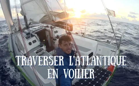 Un homme souriant sur un voilier navigue sur l'océan au coucher du soleil. Quel bateau pour traverser l'Atlantique ? Ce voilier semble prêt pour l'aventure.