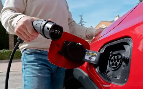 Persona desconectando el cargador de un coche eléctrico rojo.