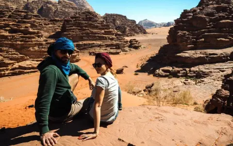 Para w turbanach odpoczywa na piasku, podziwiając skaliste krajobrazy pustyni Wadi Rum.