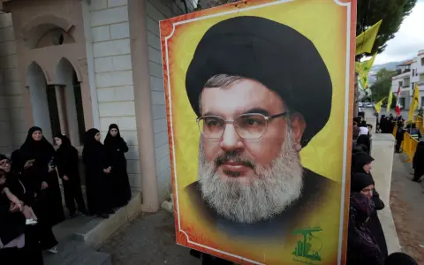 Wielki portret Hassana Nasrallaha, lidera Hezbollah, obok grupy kobiet w czarnych hidżabach.