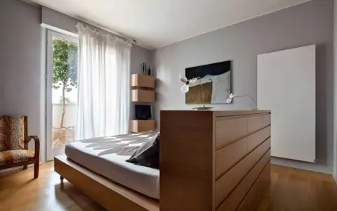 Un moderno **letto in mezzo alla stanza**, con un copriletto a motivi floreali, accanto a una poltrona leopardata e una cassettiera in legno.