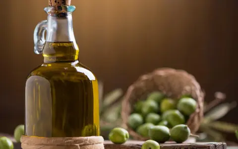 Bottiglia di olio extravergine d'oliva accanto a olive verdi, per capire la differenza tra olio di oliva e olio extravergine.