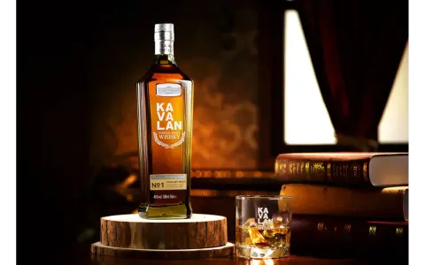 Butelka Kavalan Single Malt Whisky, uznawana za najlepszą polską whisky, obok szklanki z lodem i sterty książek.