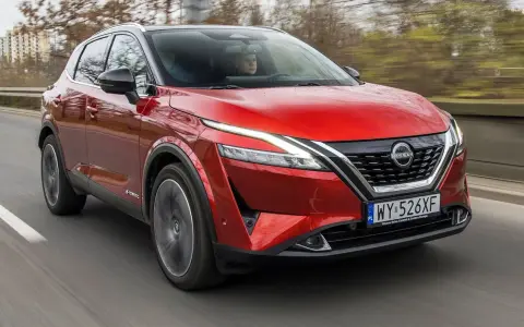 Czerwony Nissan Qashqai 2023 z napędem e-POWER jedzie po drodze, za kierownicą siedzi kierowca.