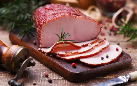 Pokrojona szynka wieprzowa z rozmarynem i pieprzem na desce.