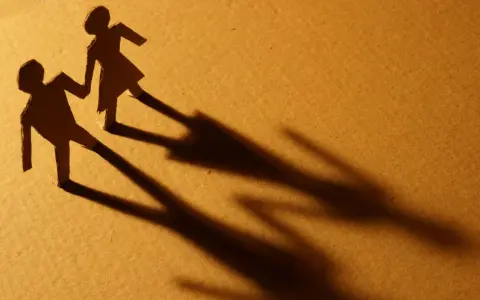 Zwei Papierfiguren, die sich an den Händen halten. Eine Figur scheint sich abzuwenden, während die andere bleibt. Sie sind noch verheiratet und eine neue Beziehung beginnt.