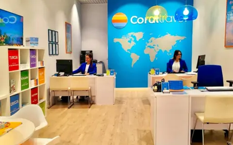 Biuro podróży Coral Travel z pracownicami za ladą i mapą świata na ścianie.