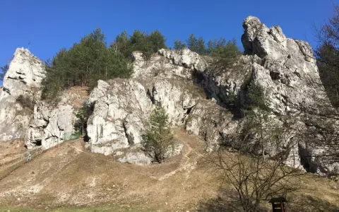 Skały wapienne i sosny w Dolinie Kobylańskiej. Ścieżka wije się po zboczu, a w oddali widać turystów.