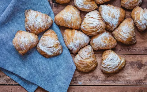 Sfogliatelle, un delizioso cibo tipico napoletano, cosparse di zucchero a velo su un tavolo di legno e un tovagliolo blu.