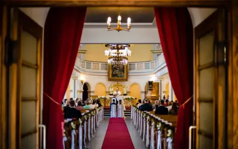 Ślub w kościele. Para młoda przed ołtarzem, ksiądz udziela im błogosławieństwa. Wszyscy zgromadzeni są chrześcijanami, a ten konkretny obrządek jest katolicki.