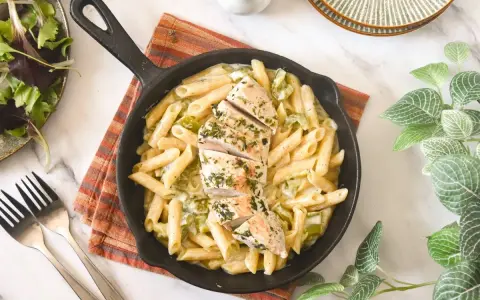 Deliciosa pasta con pollo en sartén, cubierta con hierbas frescas. Acompañada de una ensalada verde y tenedores.