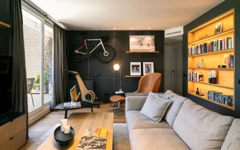 Un salón moderno con bicicleta de carretera colgada, máquina de ciclismo de madera y estanterías iluminadas. Inspiración decoración para deportistas.