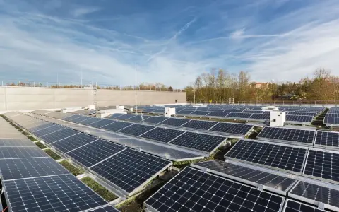 Stora fält av solpaneler på ett tak, med flera vita, små växelriktare utplacerade bland dem.