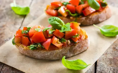 Zwei Bruschetta mit Tomaten und Basilikum, ein authentisches italienisches Rezept, auf rustikalem Holz.
