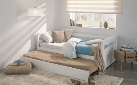 Cama nido blanca con colchones, cojines y manta en un dormitorio juvenil.