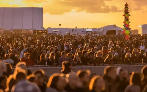 Tłum ludzi na festiwalu, zachód słońca. Kolorowa instalacja artystyczna w tle. Kto będzie następny na scenie?