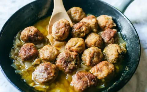 Polpette in bianco dorate e succulente, cotte in padella con cipolle dolci e un sughetto invitante.