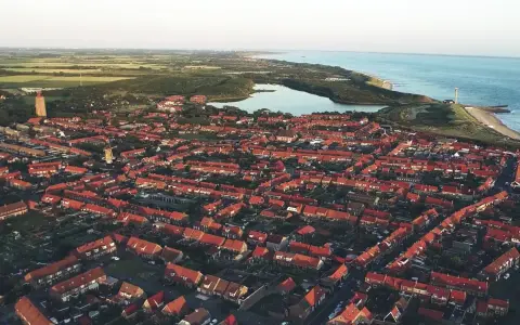Luftaufnahme einer Küstenstadt in den Niederlanden mit roten Dächern, einem Leuchtturm und dem Meer. Drohnenaufnahmen zeigen die Schönheit der Niederlande.