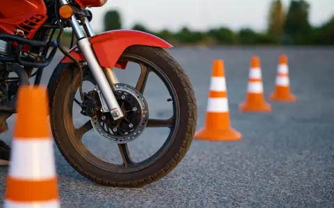 Czerwony motocykl i pomarańczowe pachołki na placu manewrowym. Przygotowanie do egzaminu na kategorie prawa jazdy na motor.