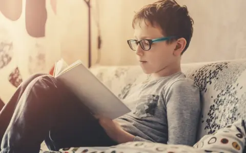 Bambino con occhiali legge un libro, concentrato su come imparare una poesia a memoria.