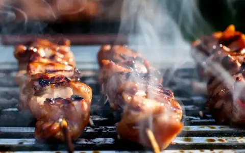 Aromatyczne yakitori skwierczy na grillu, otoczone kłębuszkami dymu.