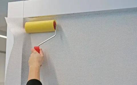 Mit einem gelben Farbroller wird eine weiße Tapete spachteln.