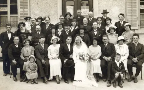 Un groupe pose pour une photo de mariage, peut-être pour un registre mariage. La mariée porte une robe blanche et un voile.
