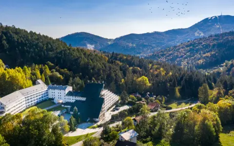 Malowniczy hotel przy stoku narciarskim w Polsce, otoczony jesiennym lasem. W oddali góry i niebo z ptakami.