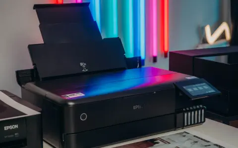 Czarna drukarka Epson z kolorowym ekranem, idealna do drukowania zdjęć. Obok stoi starszy model.