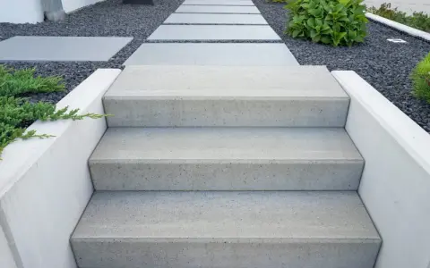 Nowe schody do ogrodu zrób sam. Nowoczesne, betonowe stopnie prowadzą przez kamienny żwirek do zieleni.