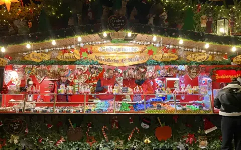 A vibrant Dresden Christmas market stall overflowing with gingerbread hearts, candied nuts, and colorful sweets. Festive lights twinkle above the tempting displays.