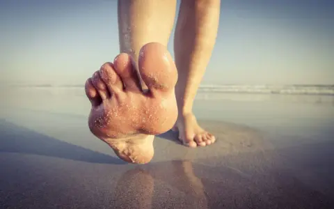 Paluch biegacza pokryty piaskiem, stopy na mokrym piasku przy plaży.