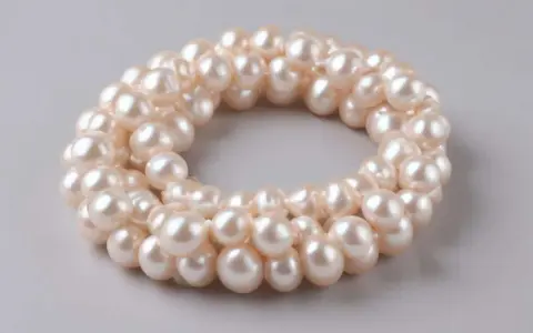 Collana di perle d'acqua dolce, simbolo di purezza e saggezza. Le perle sono disposte in un cerchio su sfondo grigio.