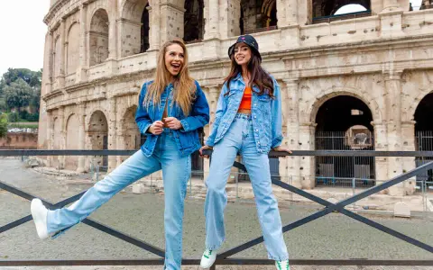 Dwie kobiety w jeans total look pozują przed Koloseum. Jedna ma rozpuszczone włosy i szeroki uśmiech, druga w kapeluszu bucket hat.