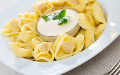 Pyszne pierożki tortellini w sosie śmietanowym, udekorowane natką pietruszki. Idealne danie na szybki obiad.
